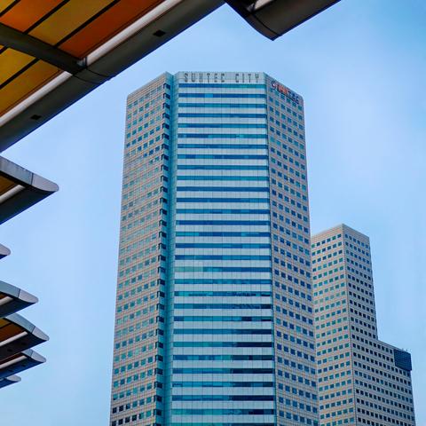 Low-angle view from under a roof structure of two office highrises against a blue sky.