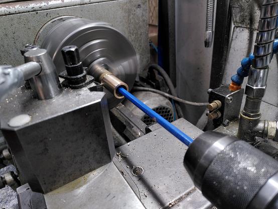 A bronze tube in the chuck of a lathe. A blue pencil is held in the tailstock chuck with the far end of the pencil disappearing into the depth of the tube.

The chuck is spinning and a parting tool can just be seen beyond the tool post.