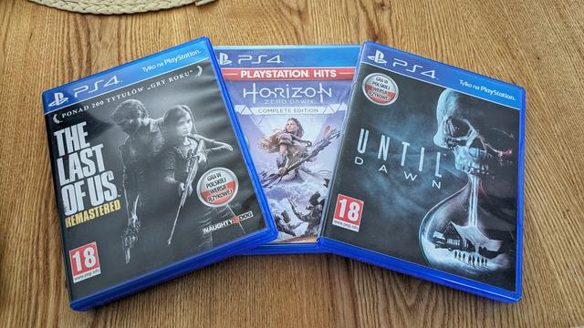 Trzy gry na PlayStation 4 na drewnianym stole: The Last of Us Remastered, Horizon Zero Dawn: Complete Edition (PlayStation Hits) oraz Until Dawn. Wszystkie w polskiej wersji językowej, oznaczone kategorią wiekową 18+.