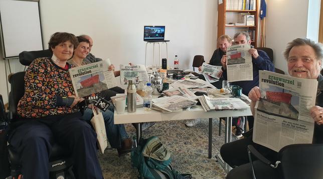 Mehere Menschen sitzen an einem Tisch mit viel Papier, Computer, Essen. Sie halten Ausgaben der GWR in der Hand