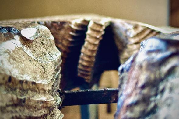 What looks to be an extreme close-up of a wooden structure somewhat resembles a kind of large canyon with massive, curved, vertical shapes cut into it in the distance and an attached horizontal, metal beam holding each side of the canyon in place.