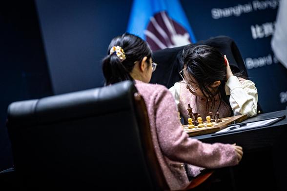 Tan Zhongyi in the foreground playing the white pieces and leaning over the board while Ju Wenjun in the background playing the black pieces with her head in her hands.

Photo by: Anna Shtourman.