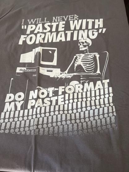 A dark t-shirt featuring a graphic of a skeleton sitting at a computer. The text reads: "I WILL NEVER 'PASTE WITH FORMATTING', DO NOT FORMAT MY PASTE!!!!!!!!!!"