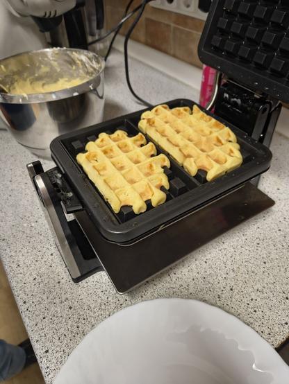 Zwei Waffeln im Waffeleisen, daneben Schüssel mit Teig