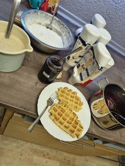 Waffeln auf Teller vor verschiedenen Toppings: Tonkabohnensauce, Sahne, verschiedene Saucen, Marmelade und ein Topf mit Heidelbeeren