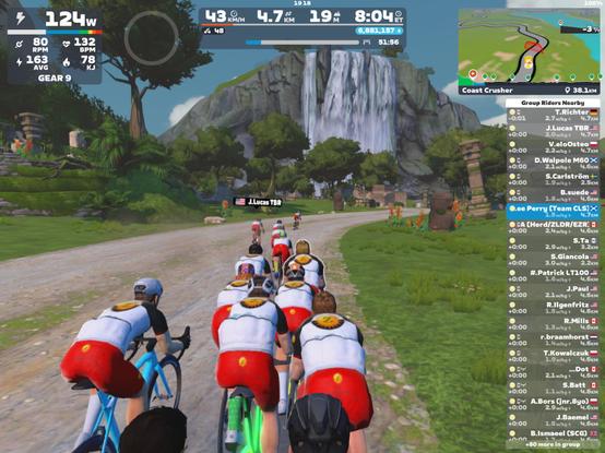 Cyclists' avatars in ZSUN kit approach a waterfall in Zwift's Watopia
