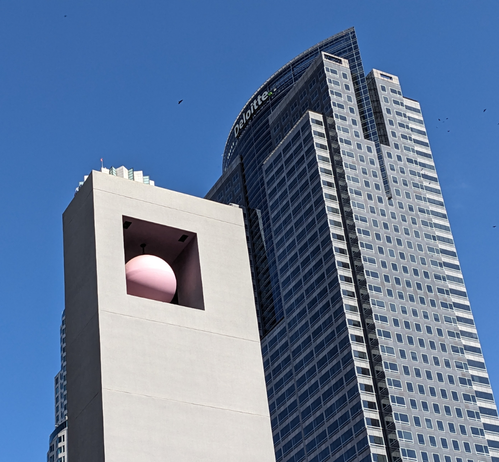 Grey tower with a red ball in it framed by a skyscraper
