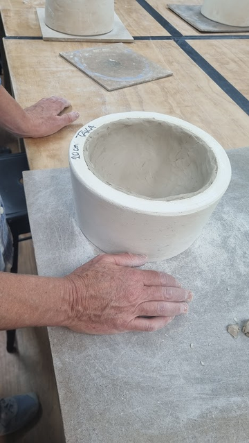 A crudely formed 25cm clay noodle pot in a plaster mould on a plywood bench in a pottery studio.