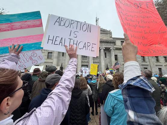 Photo of the HandsOff rally in Philadelphia, Saturday 5 April, by Katie Bernard for the Philadelphia Inquirer. A foreshortened view highlights a trans pride flag, an "Abortion is Healthcare" sign, and a sign reading 
"Hands Off 
* my disabled child
* my gay children
* my elderly parents
* my neighbors
* my personal information
* my health
* my money
* AMERICAN DEMOCRACY"