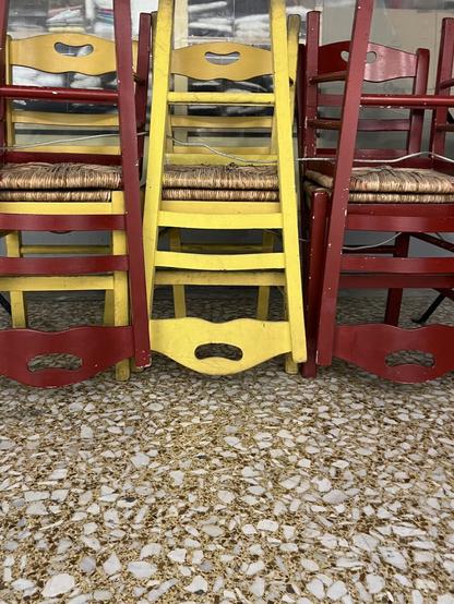 It’s the chairs of a cafe or eatery in a stoa.
 Orange and white terrazzo flooring, red chairs and yellow chairs, with straw seats, stacked in pairs