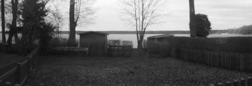 Panoramaaufnahme schwarzweiß
Seeufer, Bäume, mit Hecken geteilte Grundstücke, eine kleine Hütte.