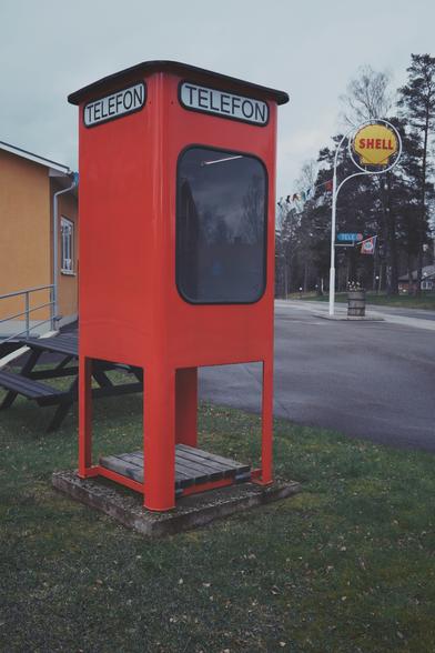 En klassisk röd telefonkiosk framför en gammal Shell bensinmack en grå aprilmorgon.