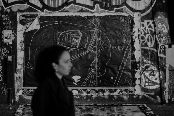 Une femme passe devant un mur ou des affiches et des graffitis se côtoient et se superposent. Photographie noir et blanc.