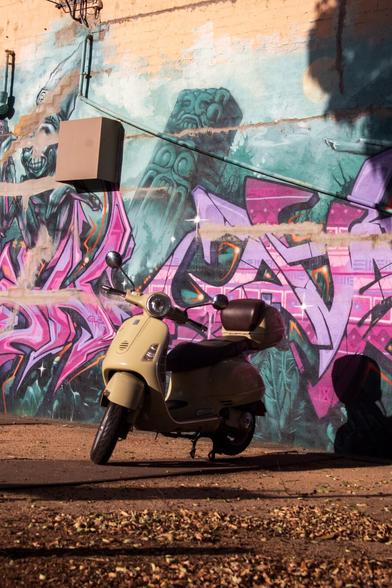 A Vespa parked in front of a brick wall covered in vivid street art and tags