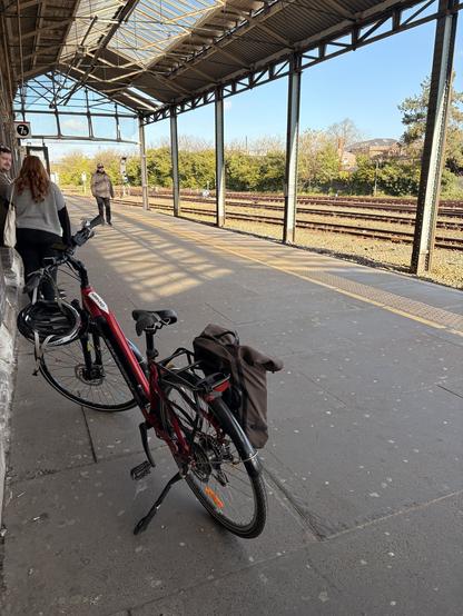 My bike on a station platform waiting for a train. Sunny blue skies beyond the platform!