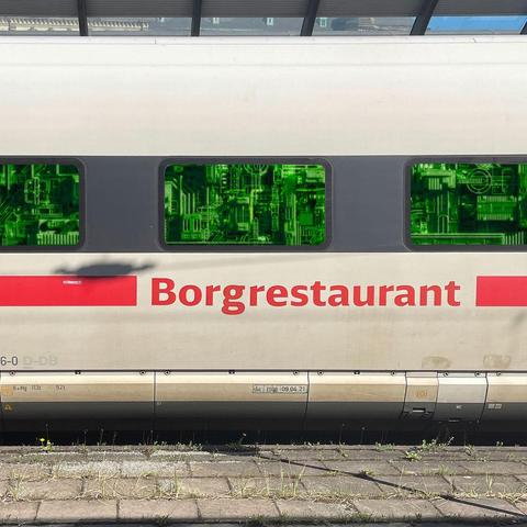 Retuschiertes Foto eines ICE am Bahnsteig, gezeigt wird der Wagen das Bordrestaurants mit der typischen Beschriftung. Darin wurde das d gegen ein g ausgetauscht, so dass es nun  Borgrestaurant heißt. Hinter den Fensterscheiben wurde eine technische Struktur eingefügt, die grün beleuchtet ist.
