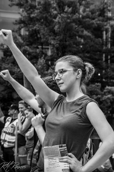 Photograph of a woman and man standing at a 2018 counterprotest in Washington DC with fists raised salute. The Unite the Right protest in DC only drew about 30 protesters, but thousands of people turned out to counter their message of hate.