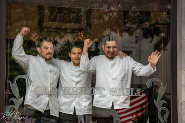 Three members of a restaurant's waitstaff in Washington DC stand inside at the front window demonstrating solidarity with the counter protest marchers in the street outside.
