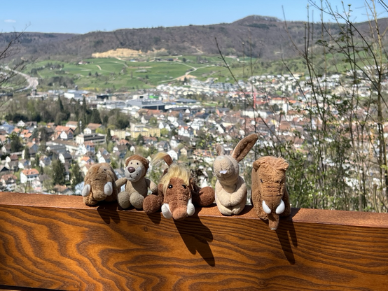 Die drei plüschigen Mammuts, Ludwig und Hopps auf einer Bank. Der Ort im Hintergrund.