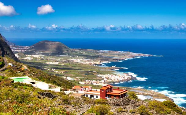 La costa nord di Tenerife, con un paese in primo piano e un cono vulcanico inattivo sullo sfondo.