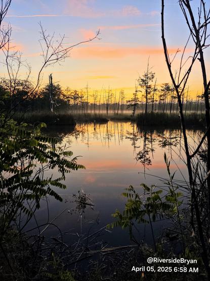Colorful sunrise rising at the horizon beyond a marshy wetland landscape and reflecting onto the quiet waterway below.