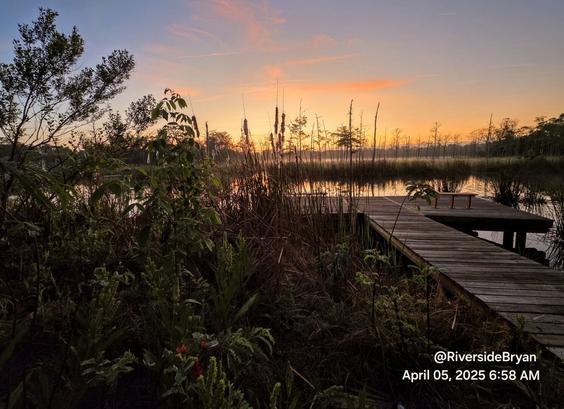 Colorful sunrise rising at the horizon beyond a marshy wetland landscape and reflecting onto the quiet waterway below.