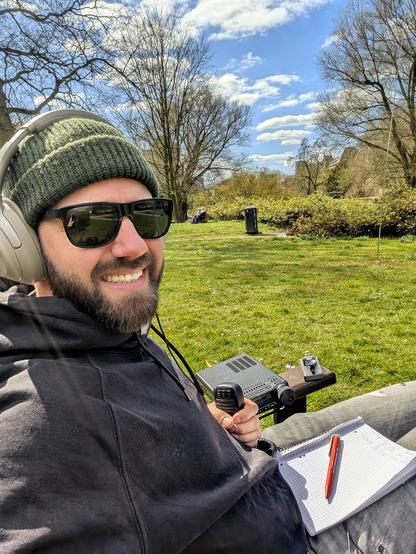 Me sitting in a chair in the park. Paper logs on the lap. The transceiver is sitting on the armrest. In the background one can see the vertical antenna.