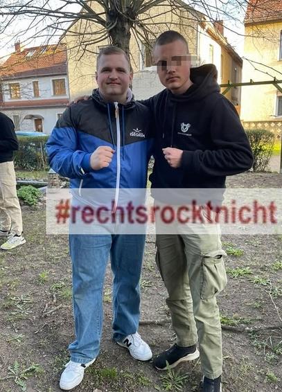 Selfie von Instagram. Dominik Kavalier Raupbach in blauer Trainigsjacke von Isegrim und ein Fan in schwarzem Hoodie stehen im Biergarten der Gaststätte Burgblick. Jeder ballt je eine Faust. Im Hintergrund sind zwei gelbe und ein weißes Haus zu erkennen, die gegenüber des Biergartens des 'Burgblick' liegen. 
Unkenntlichmachung des Gesichts des Fans ist nicht von mir, Wasserzeichen #rechtsrocktnicht aber schon.