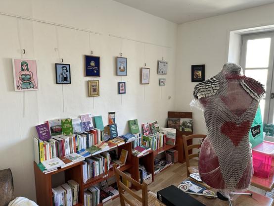 Au premier plan, un mannequin porte une armure rouge et argent. Sur le mur du fond, au dessus des livres, pleins de cadres de broderies