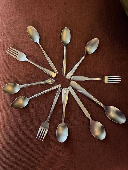 Starburst pattern formed by cutlery (spoons and forks) on a rust-colored sofa cushion. They come in various shapes and sizes, with various patterns on the part you hold.