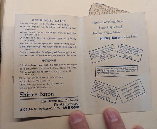 a photo of an open pamphlet, with contact information and promo material for Shirley Baron, drummer and orchestra leader, and the lyrics to the Star Spangled Banner and Hatikvah.