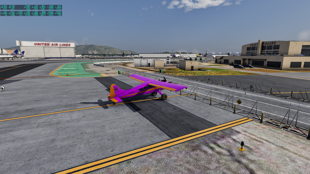 A small purple airplane is holding short a closed gate in front of a Coast Guard hanger. In the background, there is hanger with a classic red sign "United Air Lines" with at least two United Airline aircraft tails visible. Many tanks and other parked aircraft are somewhat visible in the distance. San Bruno Mountain is prominent.