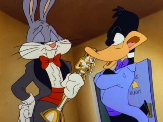 A still from a cartoon showing Bugs Bunny and Daffy Duck. Bugs is holding a golden awards statuette, and both are wearing tuxedos.