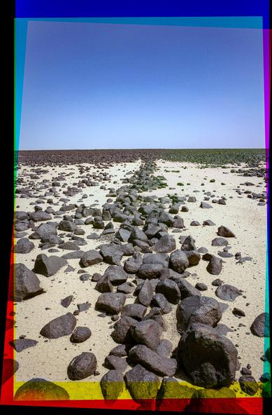 A trichrome photo showing a low line of basalt rocks in a straight line running off into the distance.