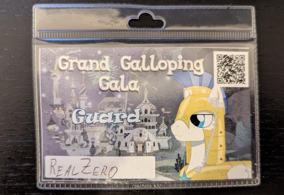 A conbadge displaying a My Little Pony royal guard pony in golden armor. Next to it is the text "Grand Galloping Gala" and the staff title "Guard".

The nickname "RealZero" is handwritten.