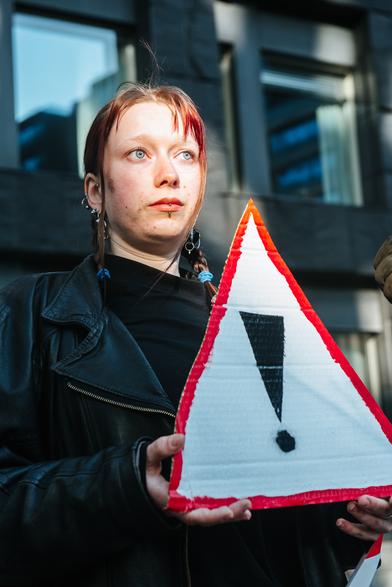 A girl standing with a triangle placard  with ! sign.