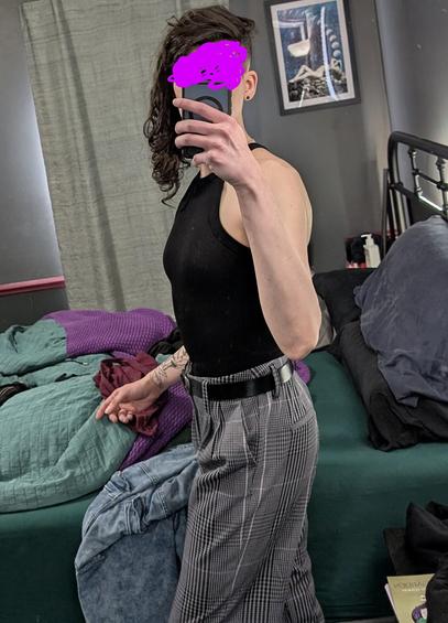 One of your favorite enbies having what is clearly a rough hair day. They are wearing a black tank, and plaid pants with a black belt. There are some clothes strewn on the bed behind them. A copy of "The Poison Garden" rests on their side-table. They are in the middle of twisting to their side, and you are able to get an excellent view of the round butt straining against the plaid pattern of the bottoms. A thin pink streak runs down part of the seams to add a flourish of color amidst the grey and white checkering.