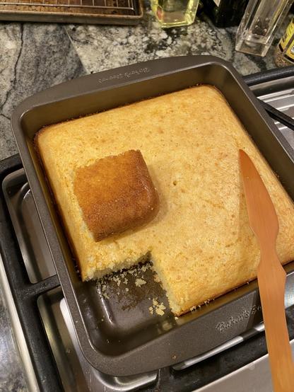 a corner piece of the cornbread cut out and laid upside down on the rest still in its pan. it’s a solid golden brown, more at corner than towards centre.