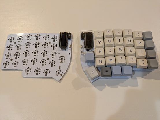 Two halves of a grey split ergonomic mechanical keyboard.  Left half is bare, a naked plate.  Right halve has keys in beige, gray and blue.