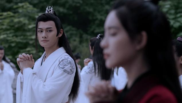 During the Mid-Autumn Festival during the lectures at the Cloud Recesses, Jiang Cheng stands with his raised hands clasped together at level with, but not pressed against, his chest. Instead of having his eyes closed to make a wish, his head is turned to look at Wen Qing who is slightly out of focus in the foreground in the pose she took for making her wish, eyes closed and hands clasped together tight against her chest just below her neck. Jiang Cheng's face shows what might be considered as a quietly wistful expression.