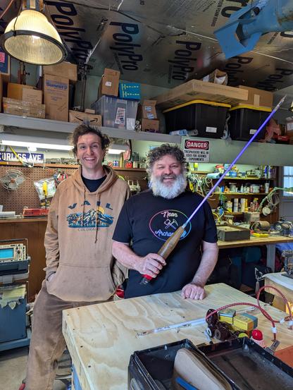 me smiling on the left in my beige Vail sweaterm and Robert on the right with a neon light saber and black and rainbow neon archaeology shirt in Roberts garage shop.
