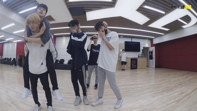 Stray Kids members in a dance practice room. Han is giving Lee Know a piggy back. Lee Know is framing Han's face with his arms and hands.