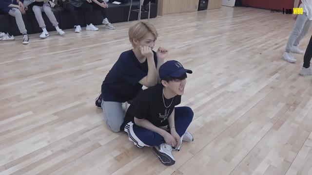 Changbin sits crosslegged on the floor of the dance practice room. Felix kneels behind him and uses his elbows to massage Changbin's back.