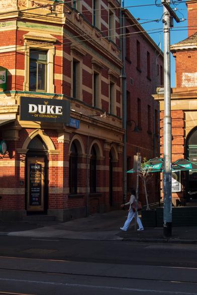 A pedestrian crosses an alley by a red brick pub lit by sunset golden light