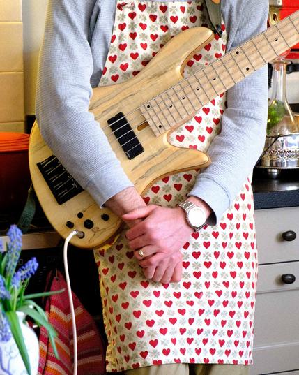 a close up of a 5-string bass guitar hanging in front of a heart-patterend apron.