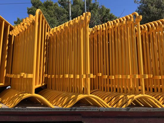 A truck bed of bright yellow barriers, metal, of the kind they put up to keep pedestrians clear of a race, in this case a cycle race.