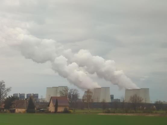an Horizont 9 Kraftwerkskühltürme von denen 4 in Betrieb sind und riesige Dampfwolken ausstoßen, die vom Wind leicht nach links weggetragen werden und sich mit den Wolken am Himmel eine Einheit bilden