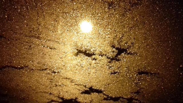Photo abstraite. Au centre un rond lumineux correspond à la lumière du lampadaire tandis que le reste de l'image n'est qu'une étendue pailletée de dorure : mon pare-brise glacé