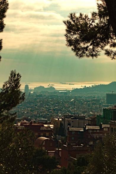 Ein Blick über eine Stadt. Im Hintergrund ist das Meer und Schiffe zu sehen. Die Sonne scheint in Straßen durch die Wolken. / A view over a city. The sea and ships can be seen in the background. The sun shines through the clouds in the streets.