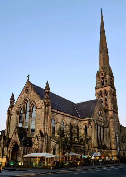 A blonde sandstone Victorian church with a very tall, slender spire.